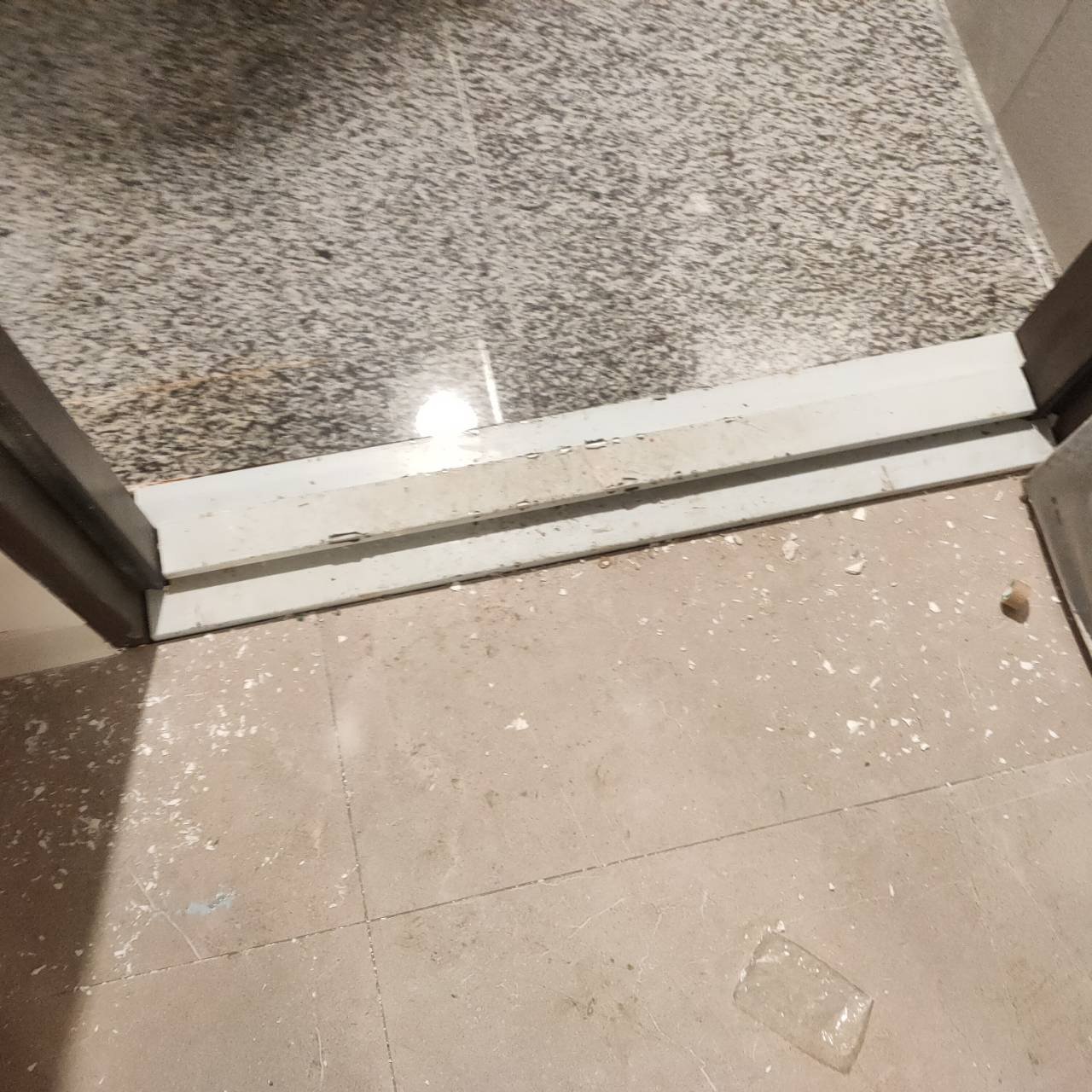 浴室門檻石材與地磚交界：收邊條上殘留膠痕與粉塵，交屋前應要求清潔或重新收邊。
