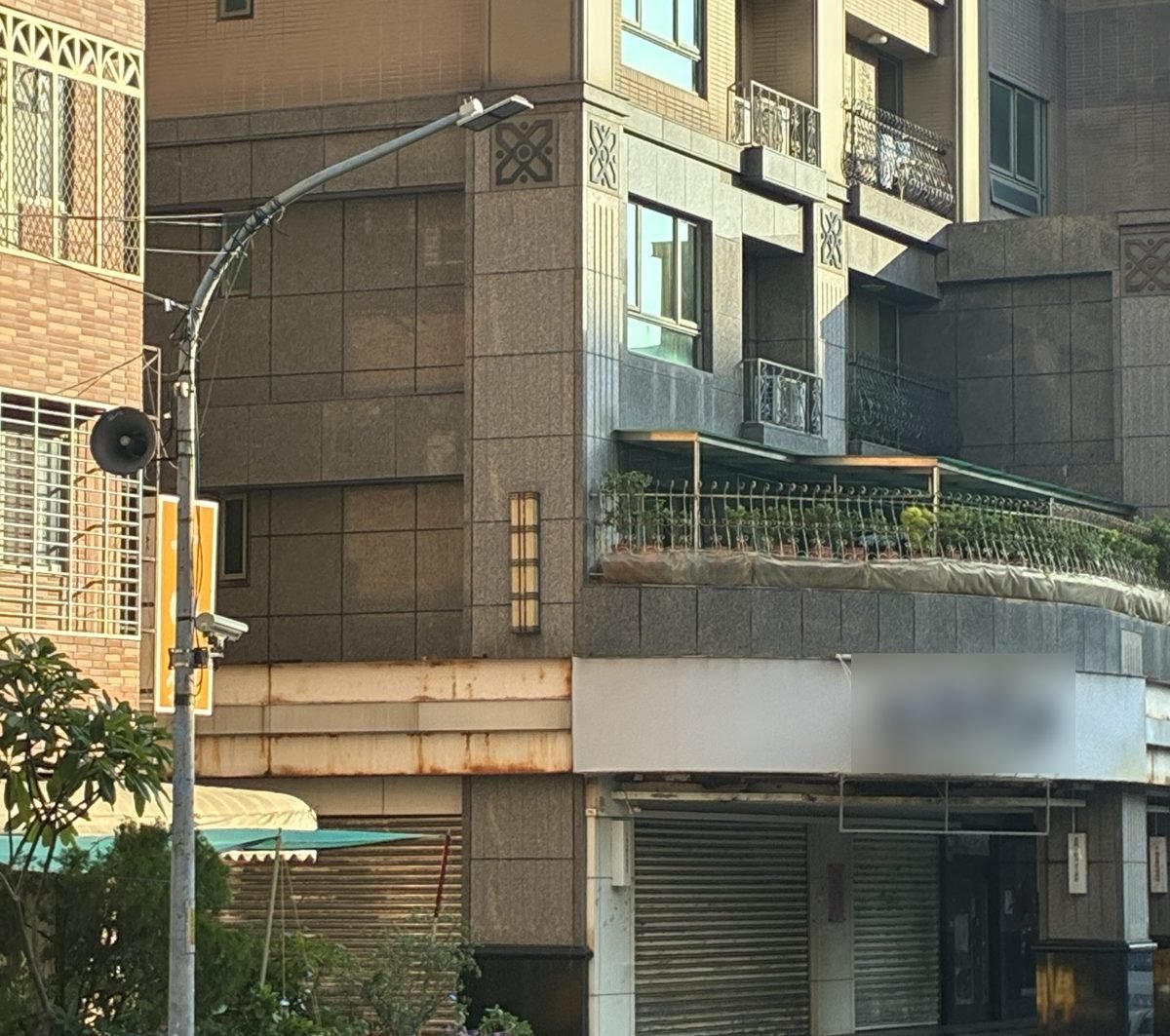 某社區 1～3 樓石材外牆：大片石材加上露台、店面，每一種交接都是可能的進水點；上方鐵件招牌框架生鏽，鏽水已流到石材面。