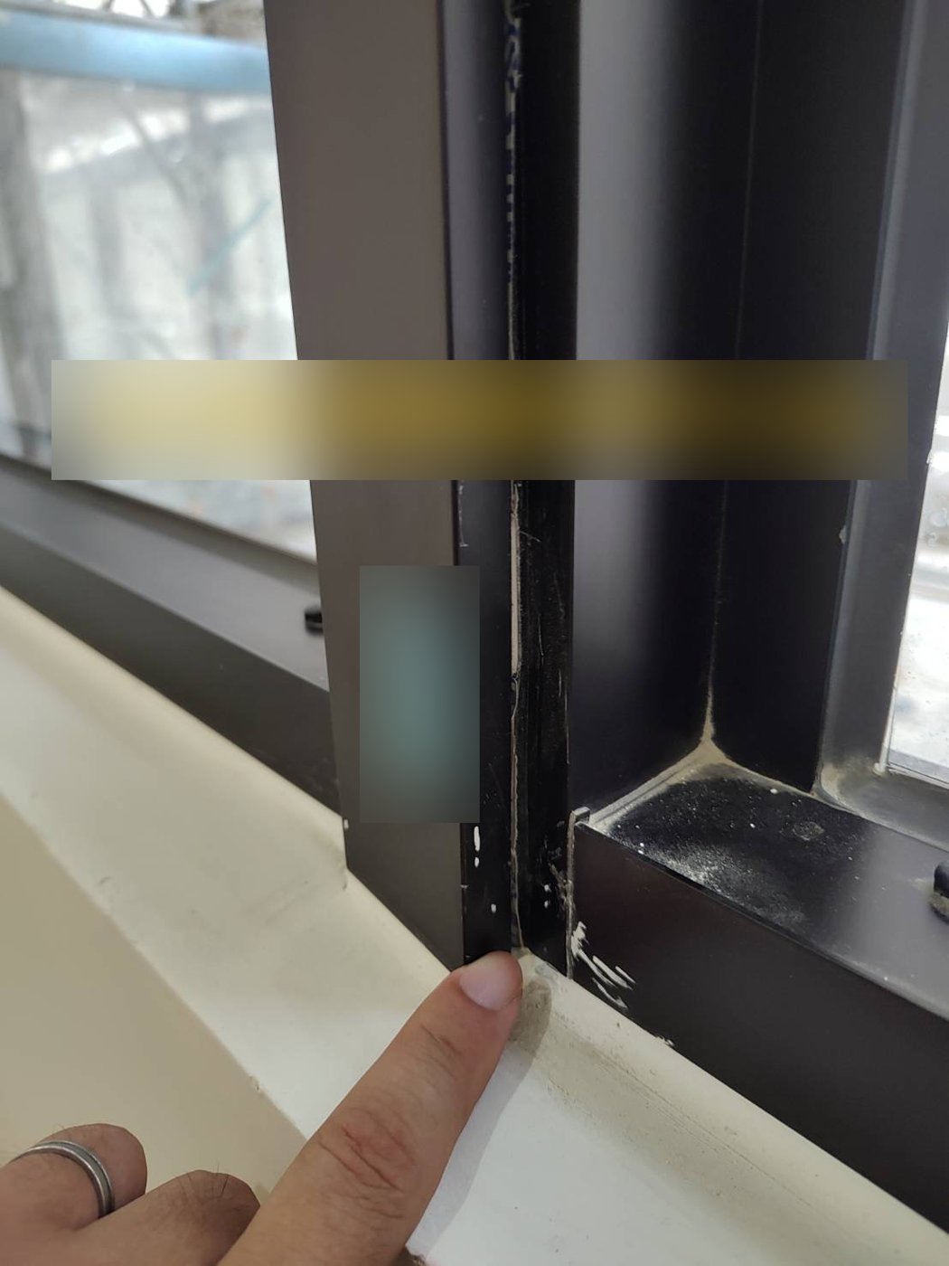 某新建案鋁窗併料處：接縫內可見縫隙與零星殘膠，屬於應在交屋前修正的缺失（標註文字已模糊處理）。